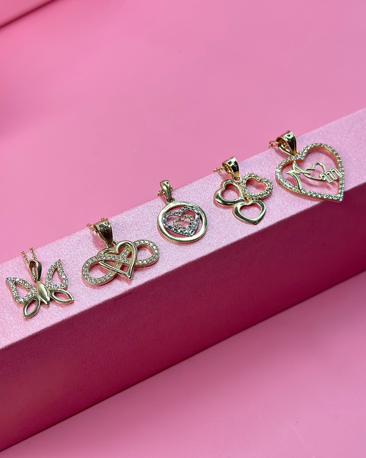 Dijes de oro con diamantes exhibidos sobre terciopelo rosa