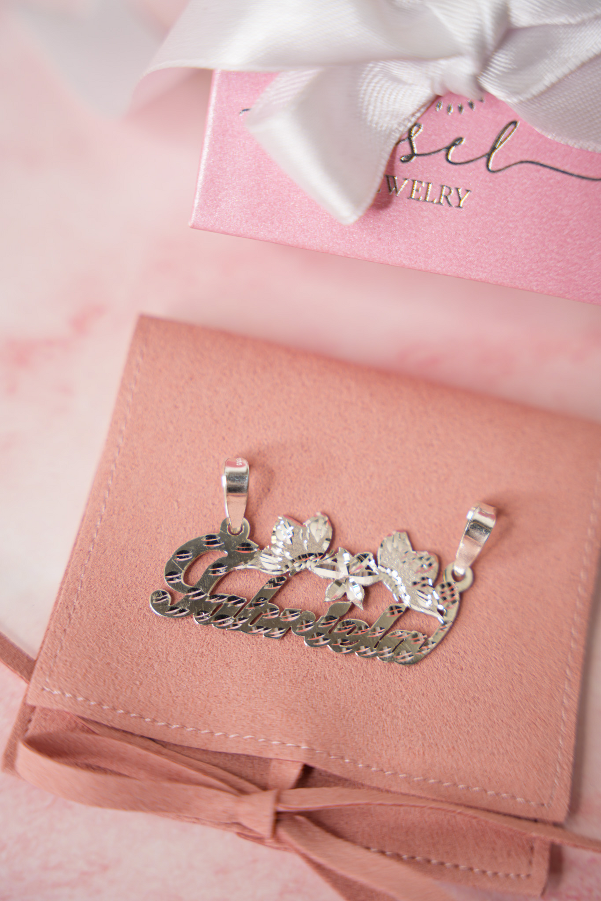 Dije personalizado con nombre en oro y diamantes sobre empaque rosa