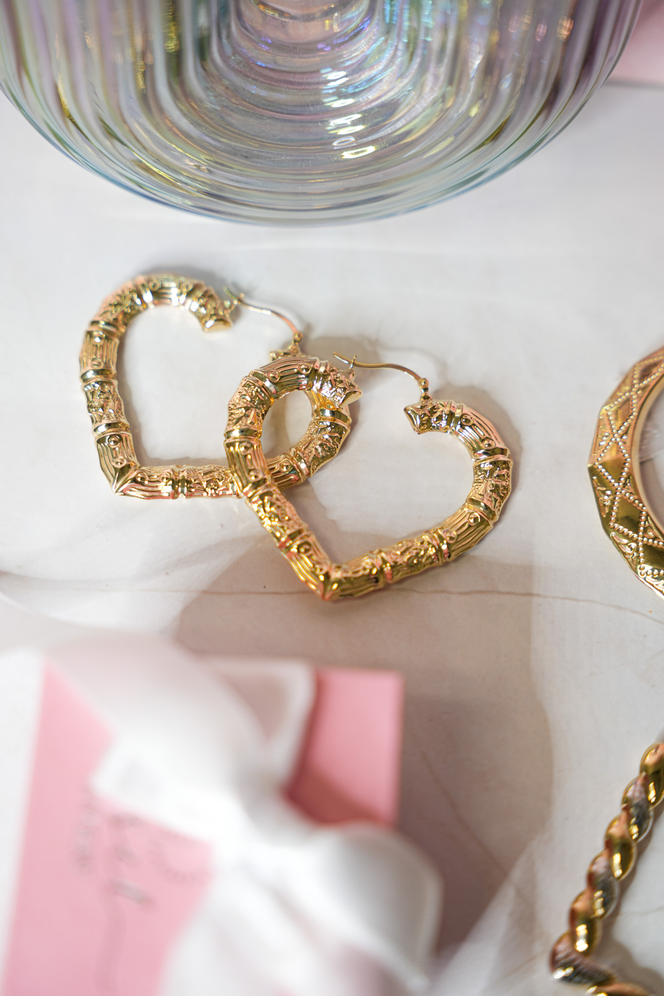 Aretes de corazón en oro junto a una bolsa de regalo rosa